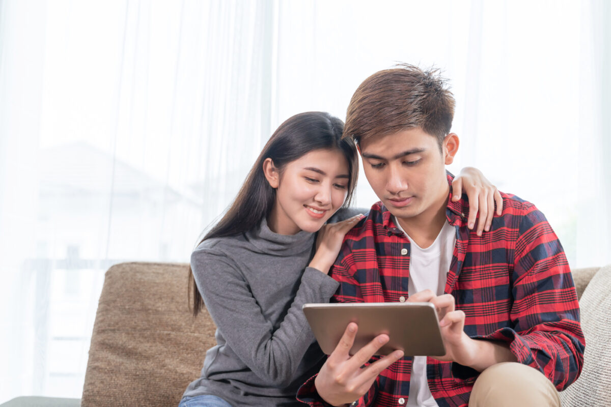 Asian young woman and handsome man sitting on couch, They happily to use smartphone together, copy space